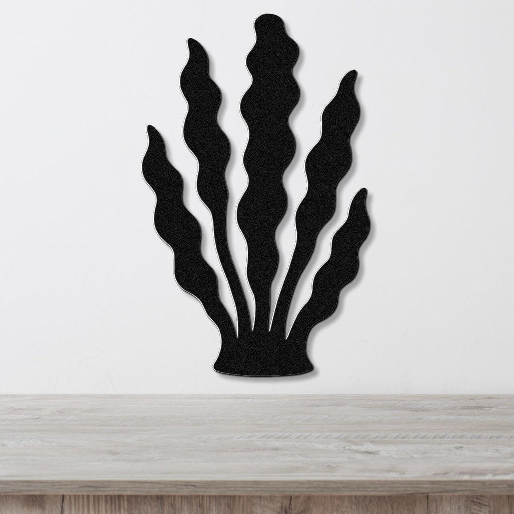 Black metal wall art in a kelp or seaweed silhouette design with wavy fronds, mounted on a white wall above a light wood surface.