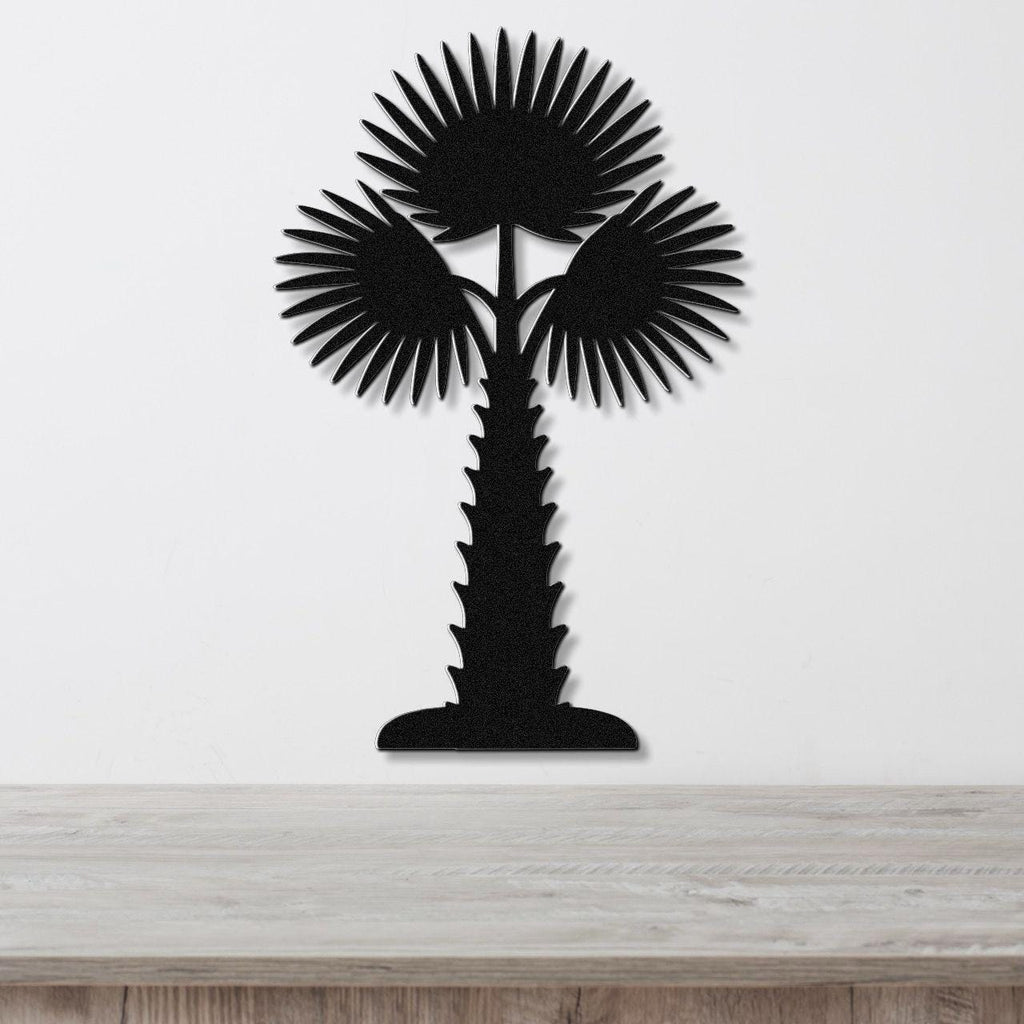 Black metal palm tree wall art with fan-shaped fronds and a textured trunk, mounted on a white wall above a light wood countertop.
