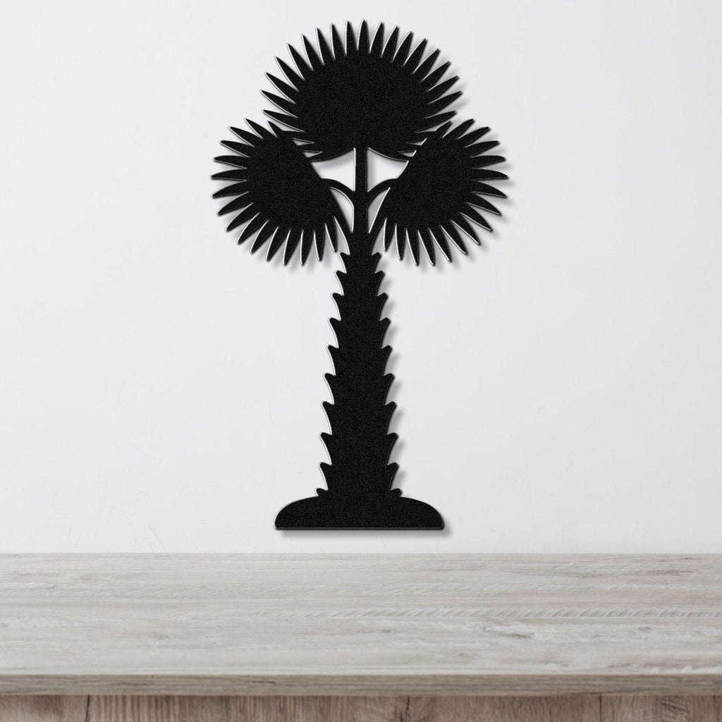 Black metal palm tree wall art with fan-shaped fronds and a textured trunk, mounted on a white wall above a light wood surface.