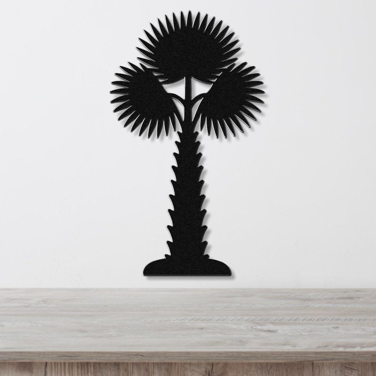 Black metal palm tree wall art with fan-shaped fronds and a textured trunk, mounted on a white wall above a light wood surface.