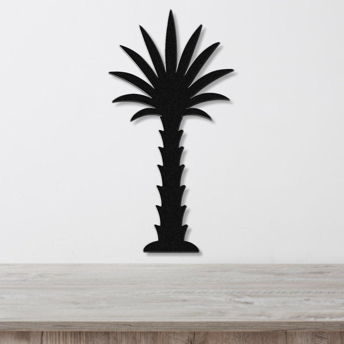 Black metal palm tree wall art with a silhouette design, mounted on a white wall above a wooden surface.