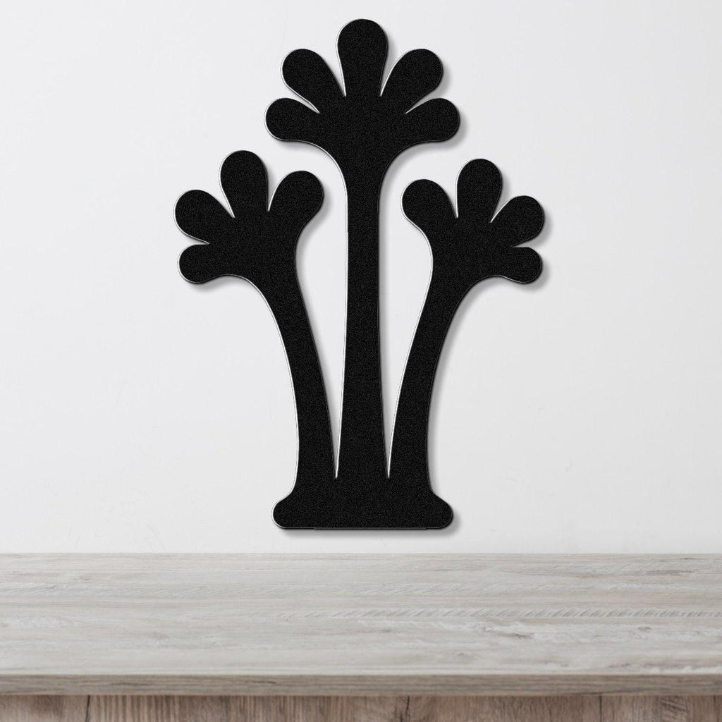 Black metal wall art in a silhouette of three abstract palm trees with fan-shaped tops, mounted on a white wall above a light wood surface.