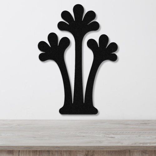 Black metal wall art in a silhouette of three abstract palm trees with fan-shaped tops, mounted on a white wall above a light wood surface.