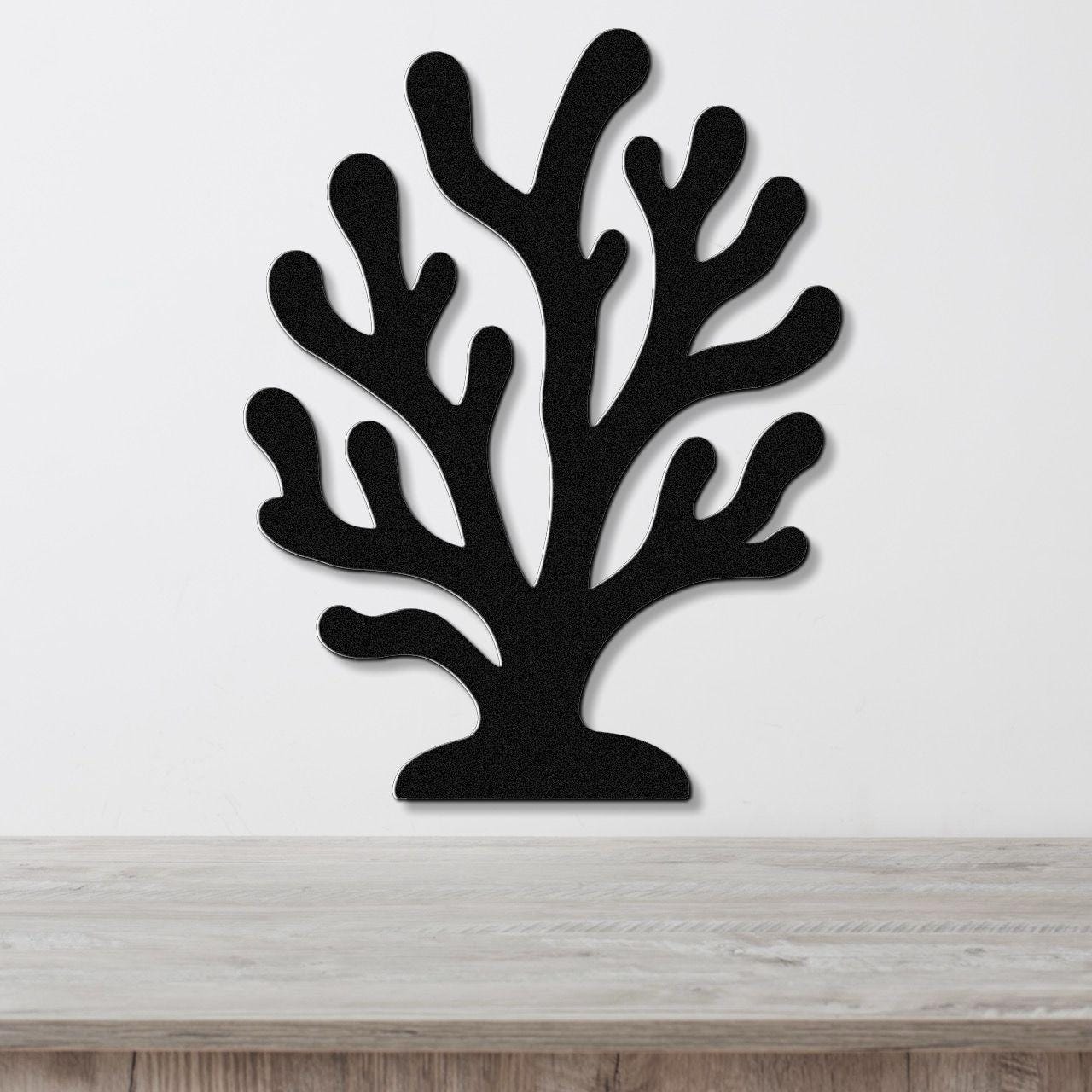 Black metal coral wall art with branching cutouts, mounted on a white wall above a light wood counter.