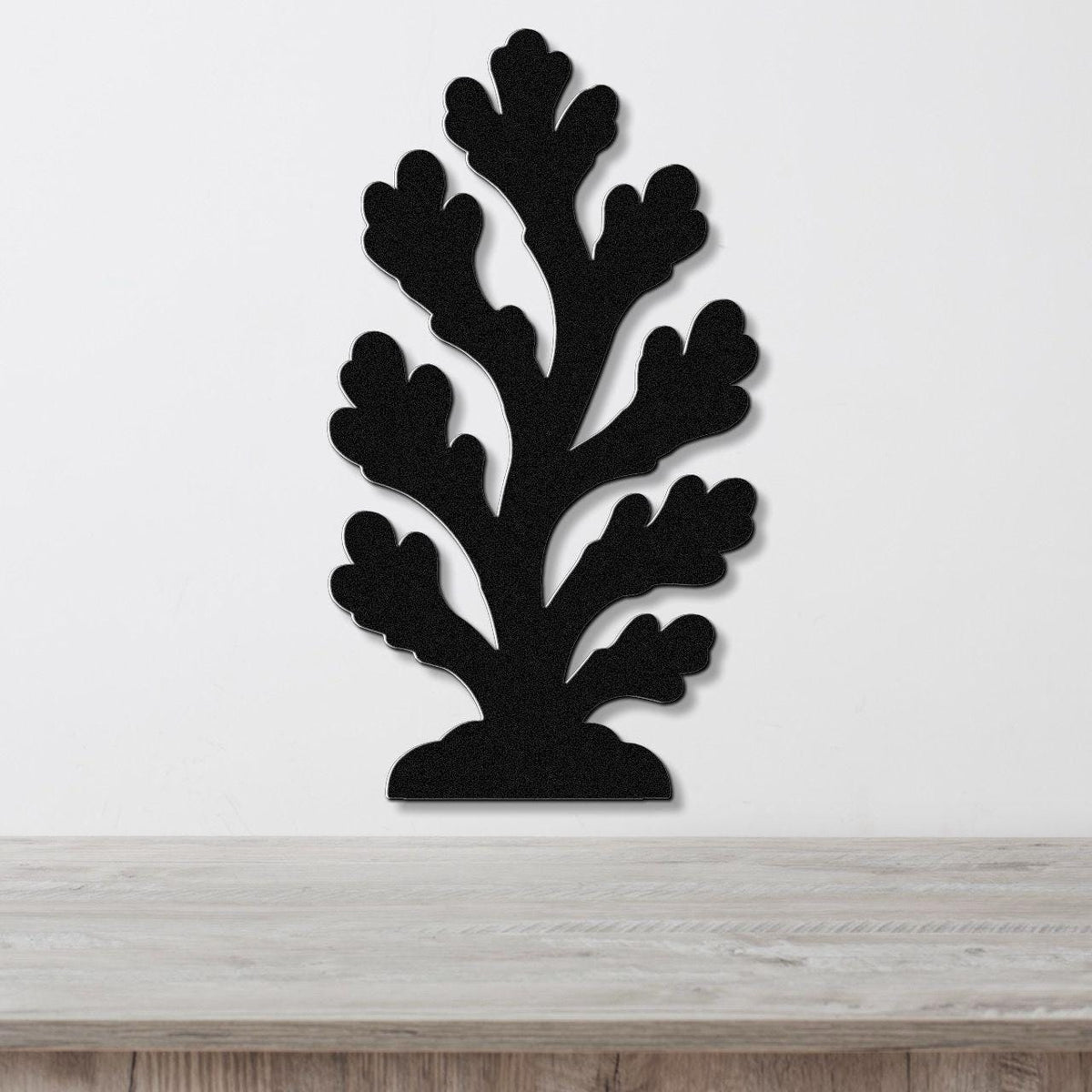 Black metal coral wall art with branching cutouts, mounted on a white wall above a light wood surface.