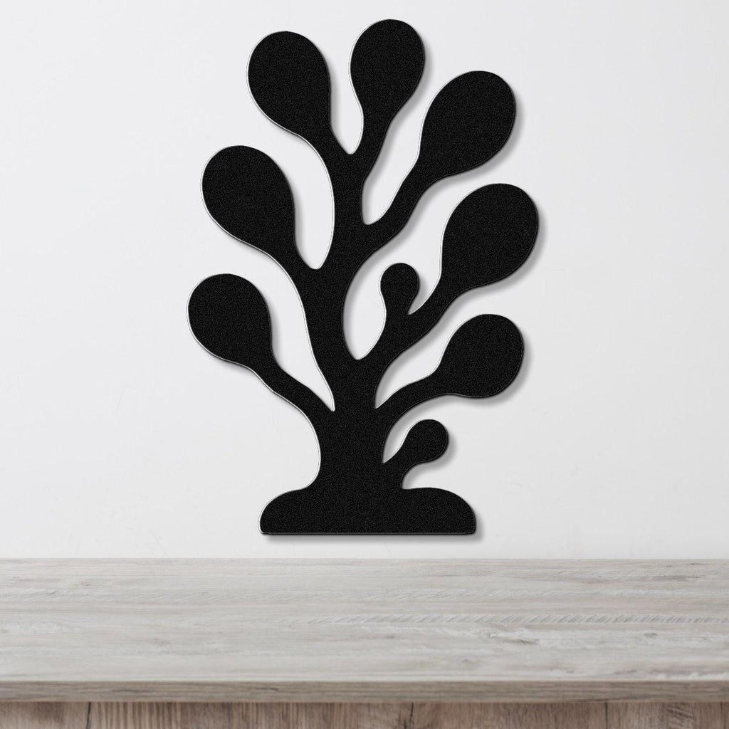 Black metal wall art in a coral or seaweed silhouette design with multiple rounded cutouts, mounted on a white wall above a light wood surface.