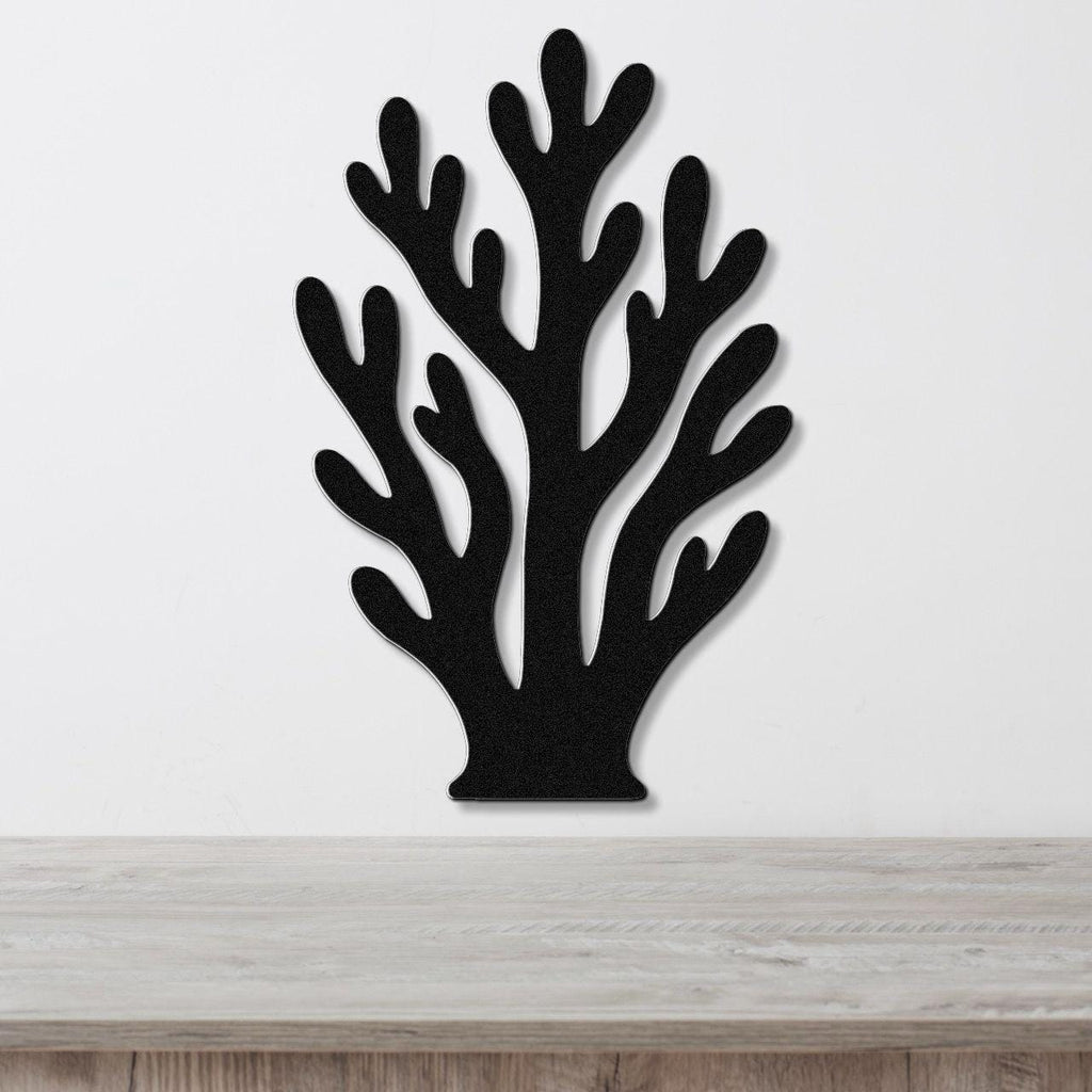 Black metal wall art in a branching coral silhouette with cutout details, mounted on a white wall above a light wood surface.