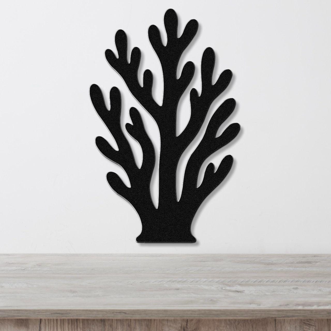 Black metal wall art in a branching coral silhouette with cutout details, mounted on a white wall above a light wood surface.