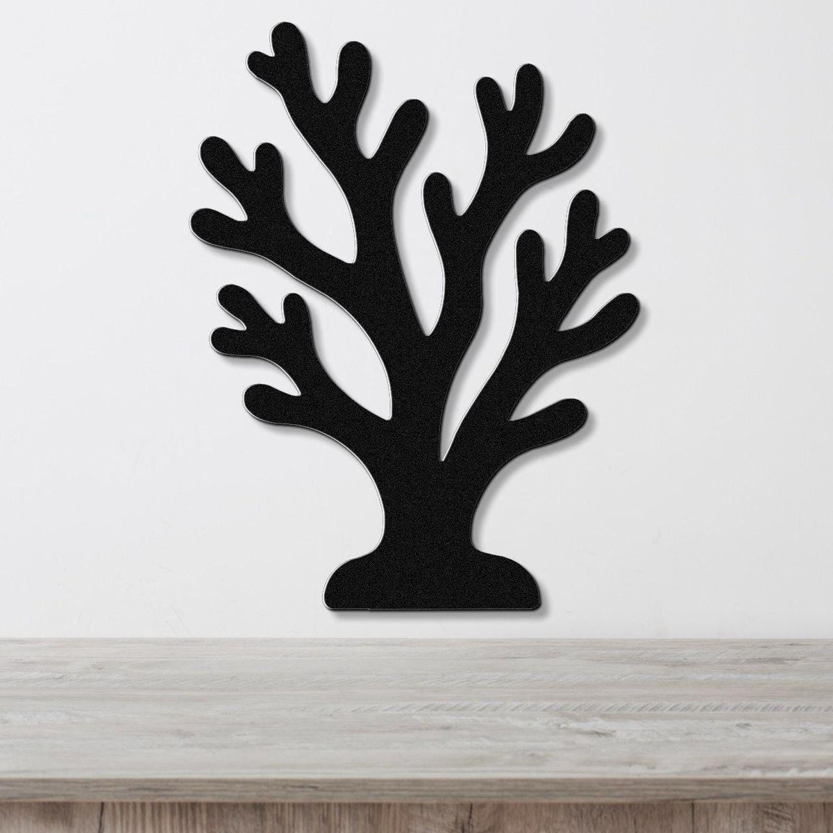 Black metal coral wall art with branching cutouts, mounted on a white wall above a light wood surface.