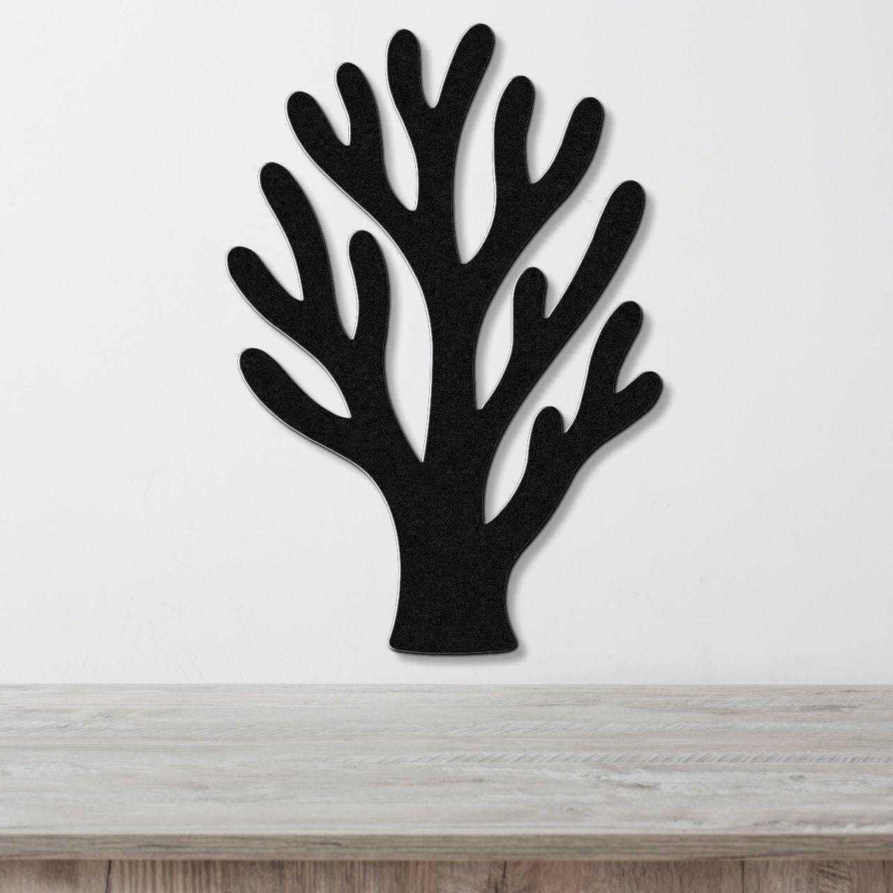 Black metal coral wall art with branching cutouts, mounted on a white wall above a light wood counter.