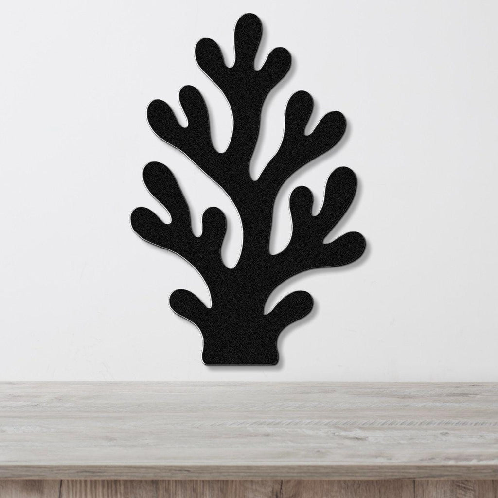 Black metal coral wall art with branching cutouts, mounted on a white wall above a light wood surface.