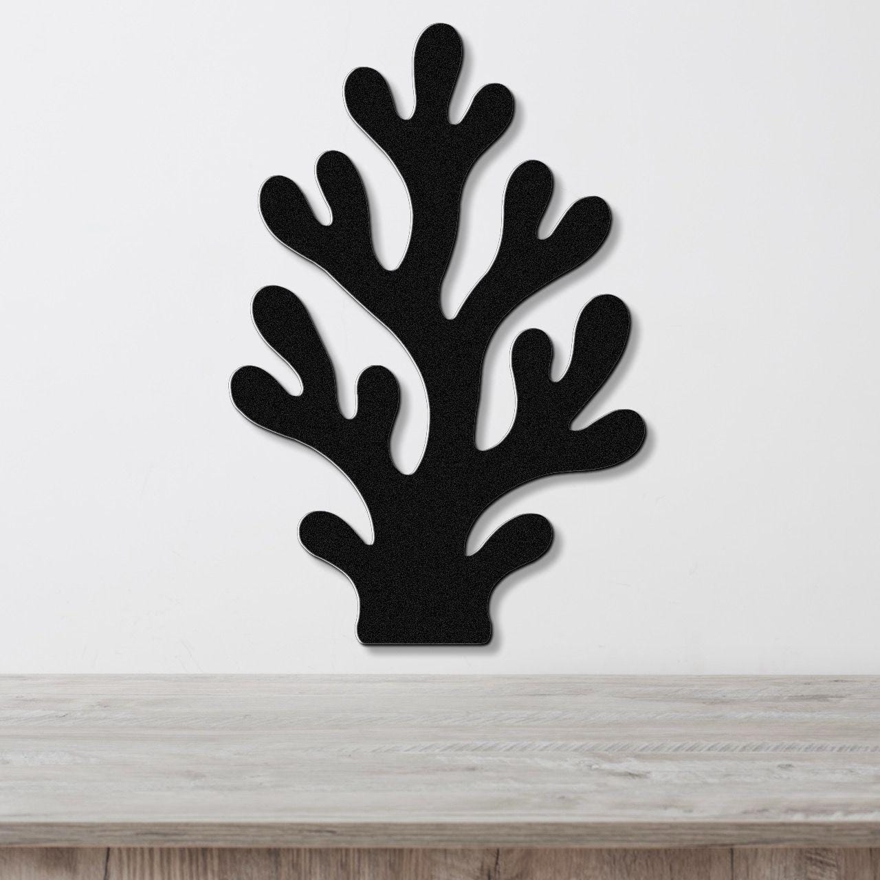 Black metal coral wall art with branching cutouts, mounted on a white wall above a light wood surface.