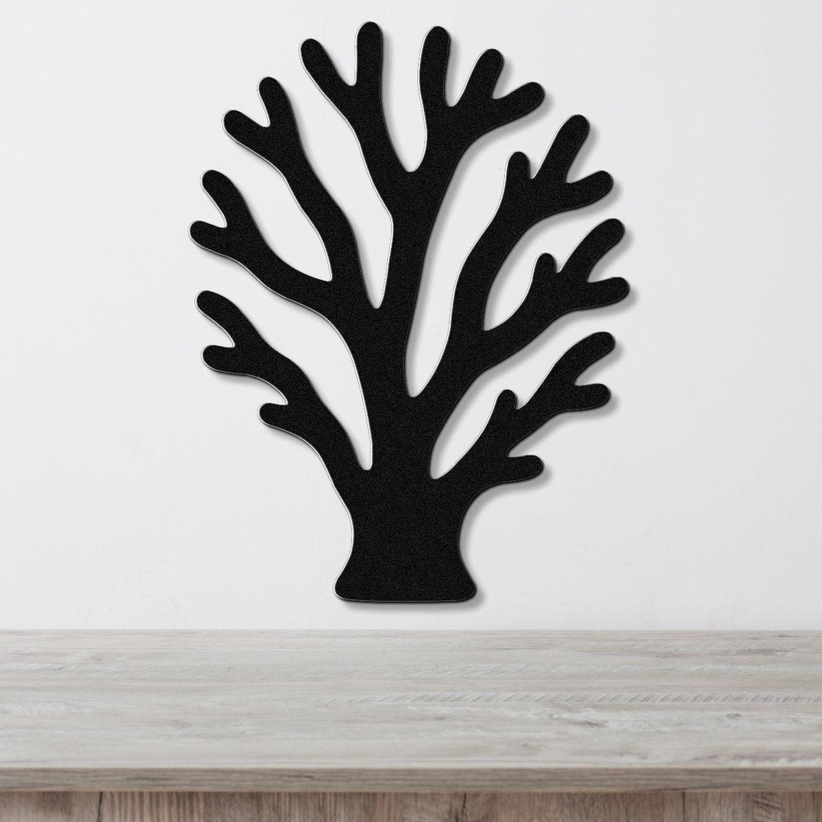 Black metal wall art in a branching coral silhouette with cutout details, mounted on a white wall above a light wood surface.