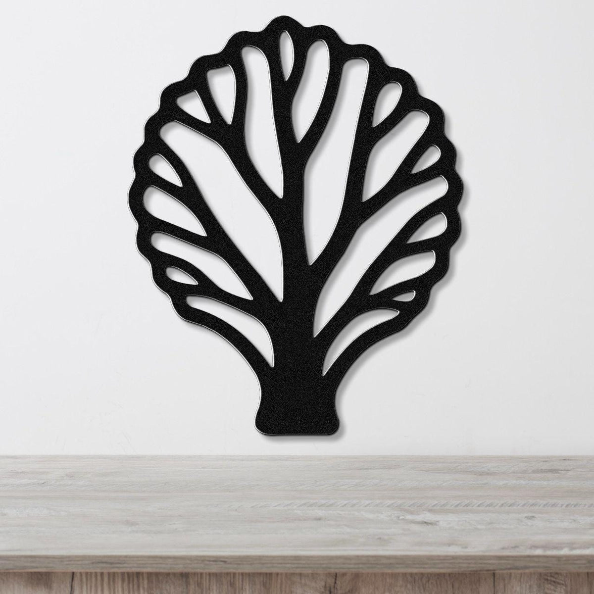 Black metal wall art in a fan coral silhouette with intricate cutout branches, mounted on a white wall above a light wood surface.