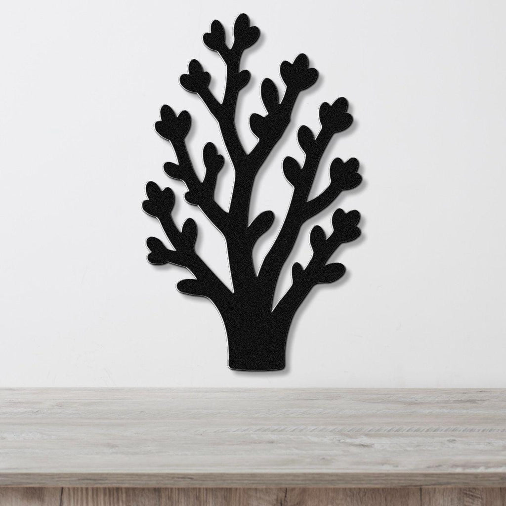 Black metal wall art in a tree silhouette with branching cutouts, mounted on a white wall above a light wood surface.
