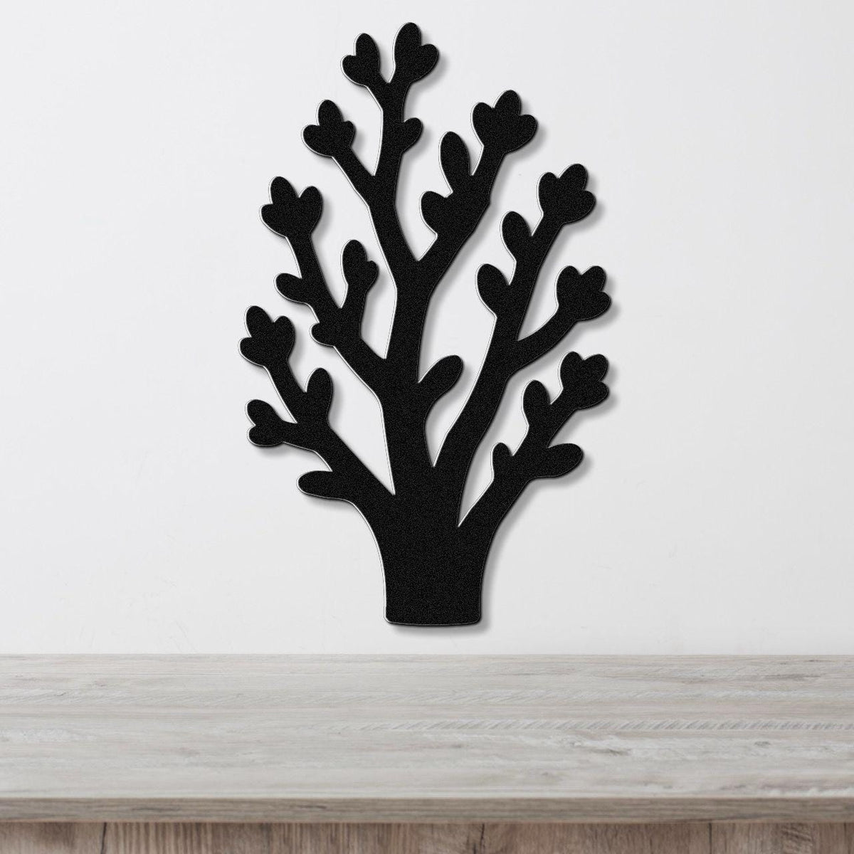Black metal wall art in a tree silhouette with branching cutouts, mounted on a white wall above a light wood surface.