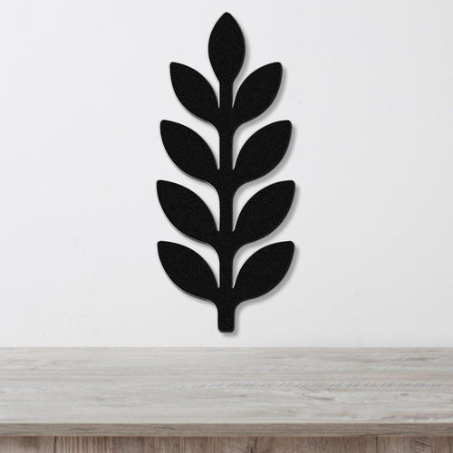 Black metal wall art in a leafy sprig silhouette with cutout details, mounted on a white wall above a light wood surface.