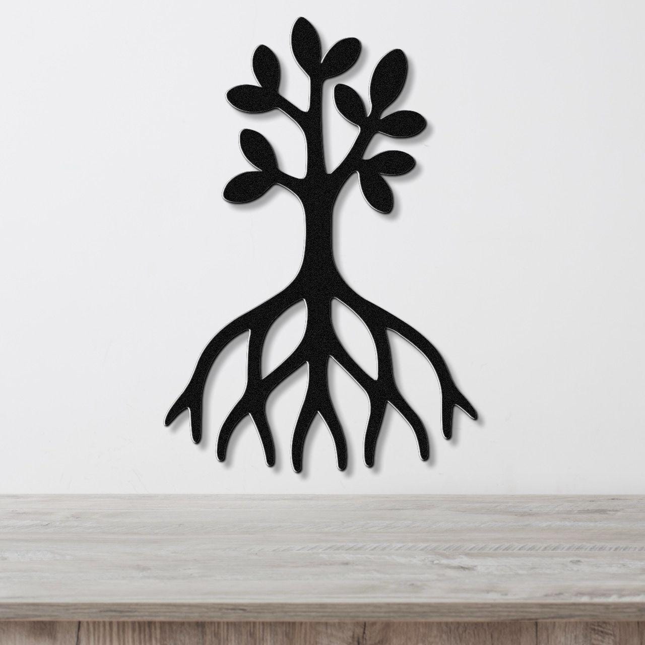 Black metal wall art cutout of a tree with visible roots and leafy branches, mounted on a white wall above a light wood surface.