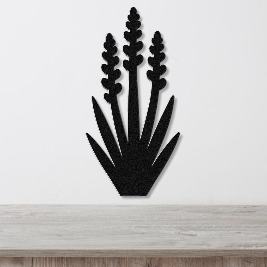 Black metal wall art in a yucca plant silhouette with three tall flower spikes and spiky leaves, mounted on a white wall above a light wood surface.