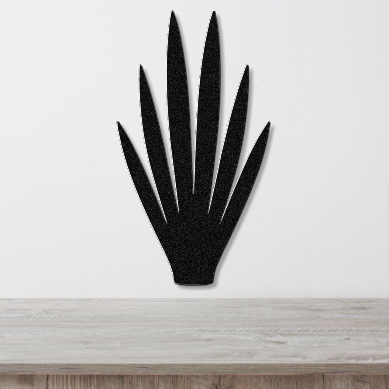 Black metal yucca wall art with pointed leaf cutouts, mounted on a white wall above a light wood countertop.