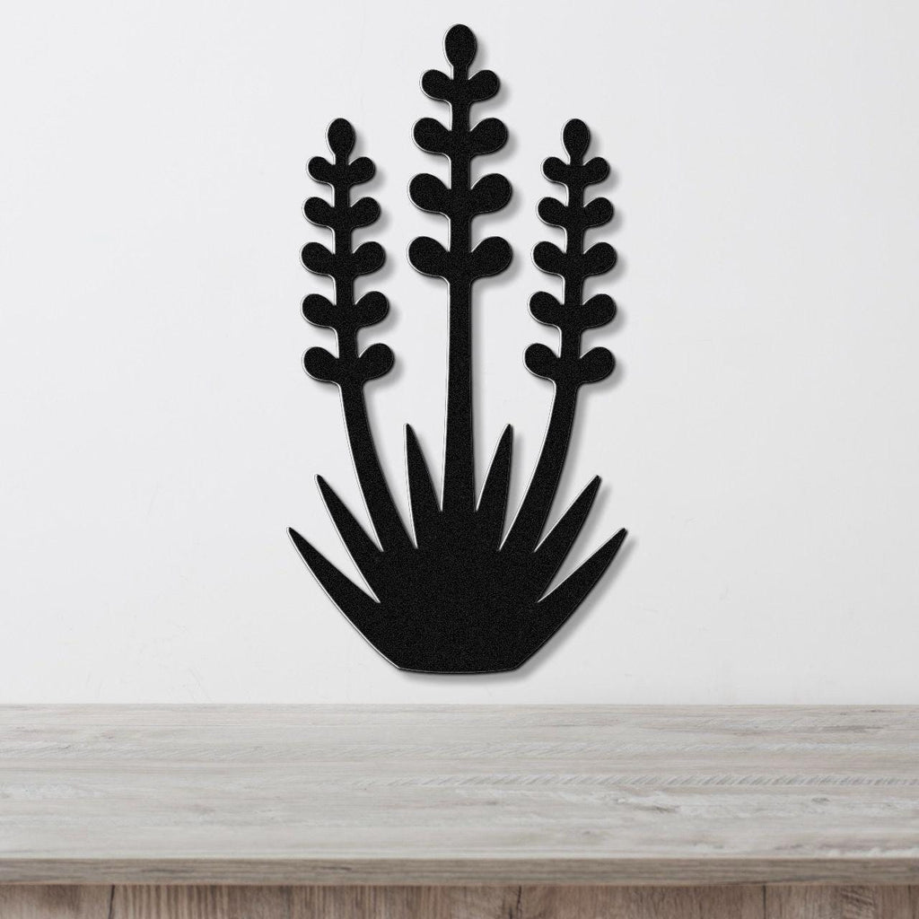 Black metal wall art cutout of a yucca plant with three tall stems and spiky base, mounted on a white wall above a light wood surface.