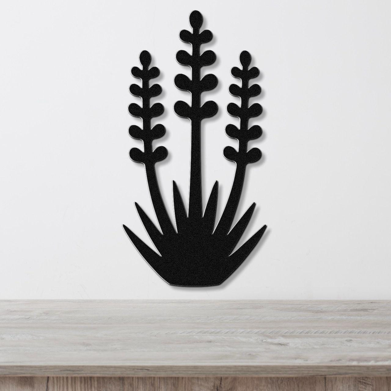 Black metal wall art cutout of a yucca plant with three tall stems and spiky base, mounted on a white wall above a light wood surface.