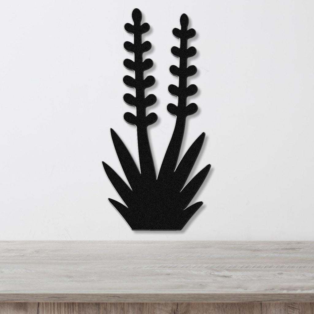 Black metal wall art in the silhouette of a yucca plant with two tall flower stalks and spiky leaves, mounted on a white wall above a wooden surface.