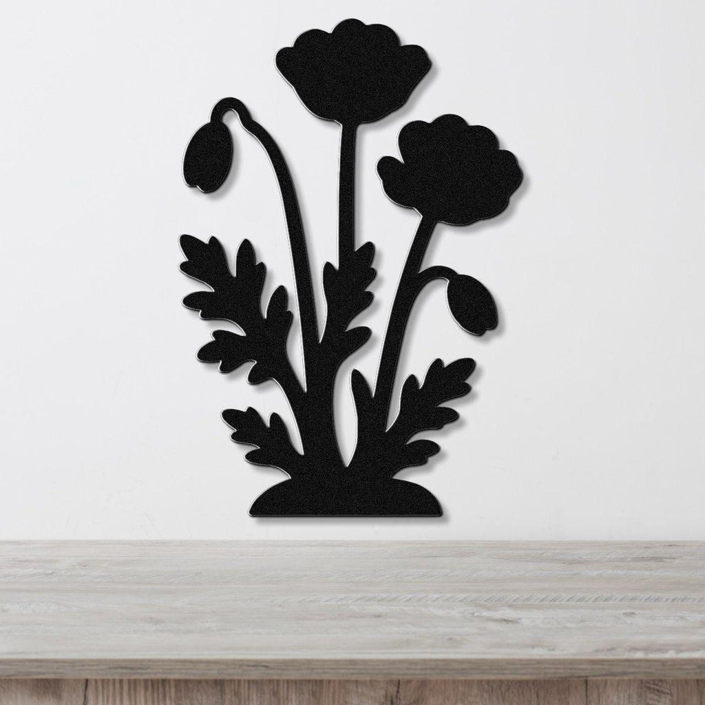 Black metal wall art featuring a silhouette of poppy flowers and leaves, mounted on a white wall above a wooden surface.