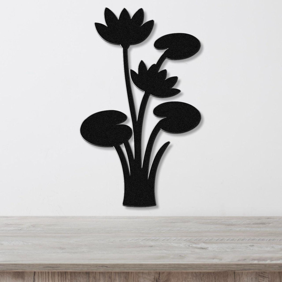 Black metal wall art featuring a lotus water lily silhouette with cutout flowers and leaves, mounted on a white wall above a wooden surface.