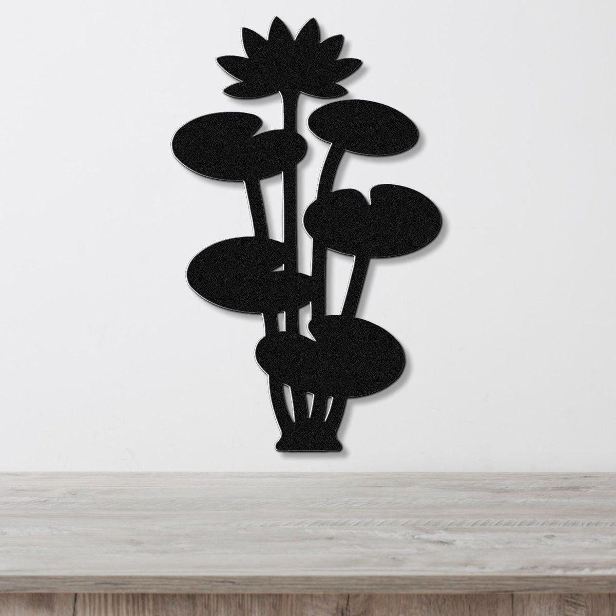 Black metal lotus water lily wall art with layered flower and leaf cutouts, mounted on a white wall above a wooden surface.