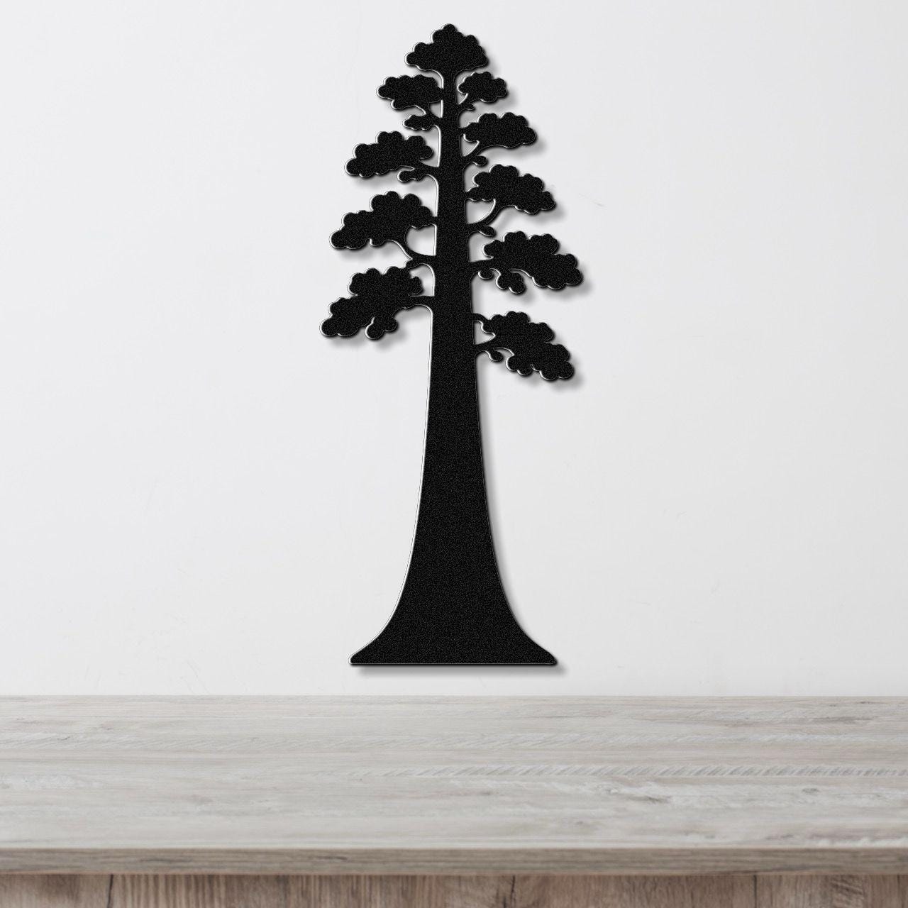 Black metal wall art cutout of a sequoia tree with layered branches, mounted on a white wall above a light wood countertop.