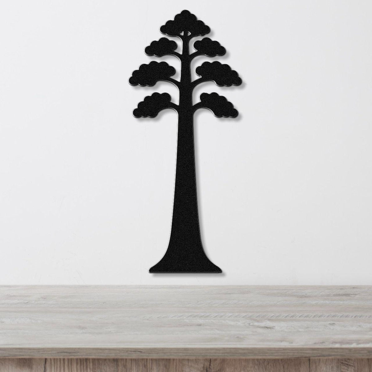 Black metal wall art in the silhouette of a sequoia tree with layered canopy cutouts, mounted on a white wall above a light wood surface.