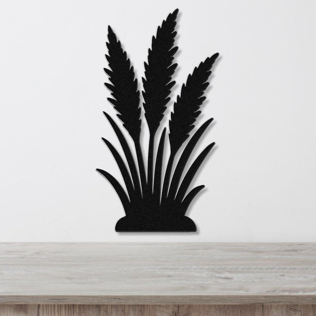 Black metal wall art in a silhouette of wild grass with layered blades and seed heads, mounted on a white wall above a light wood surface.
