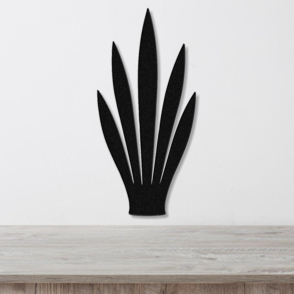 Black metal wall art in the shape of a snake plant with six pointed leaves, mounted on a white wall above a light wood surface.