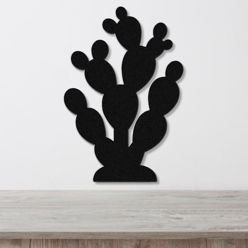 Black metal prickly pear cactus wall art with layered pads and cutout details, mounted on a white wall above a light wood surface.
