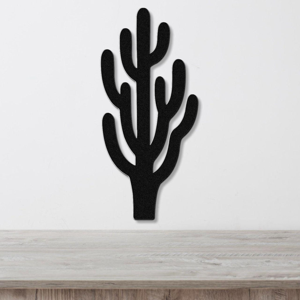 Black metal saguaro cactus wall art with branching arms and internal cutouts, mounted on a white wall above a light wood surface.