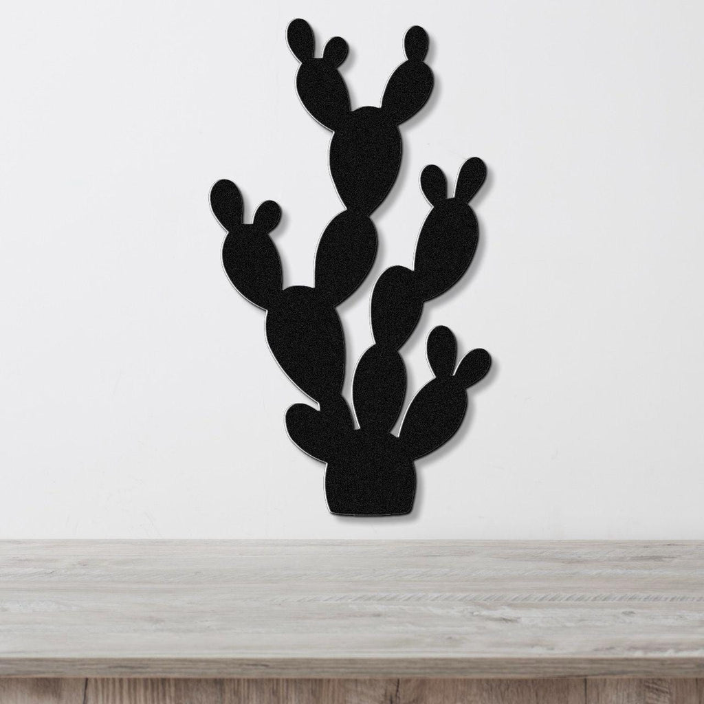 Black metal cactus wall art with multiple paddle-shaped segments, mounted on a white wall above a light wood surface.