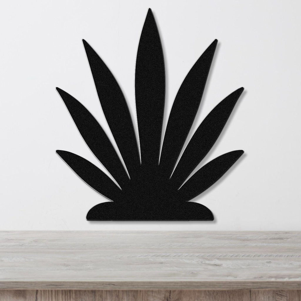Black metal agave wall art with pointed leaf cutouts, mounted on a white wall above a light wood surface.