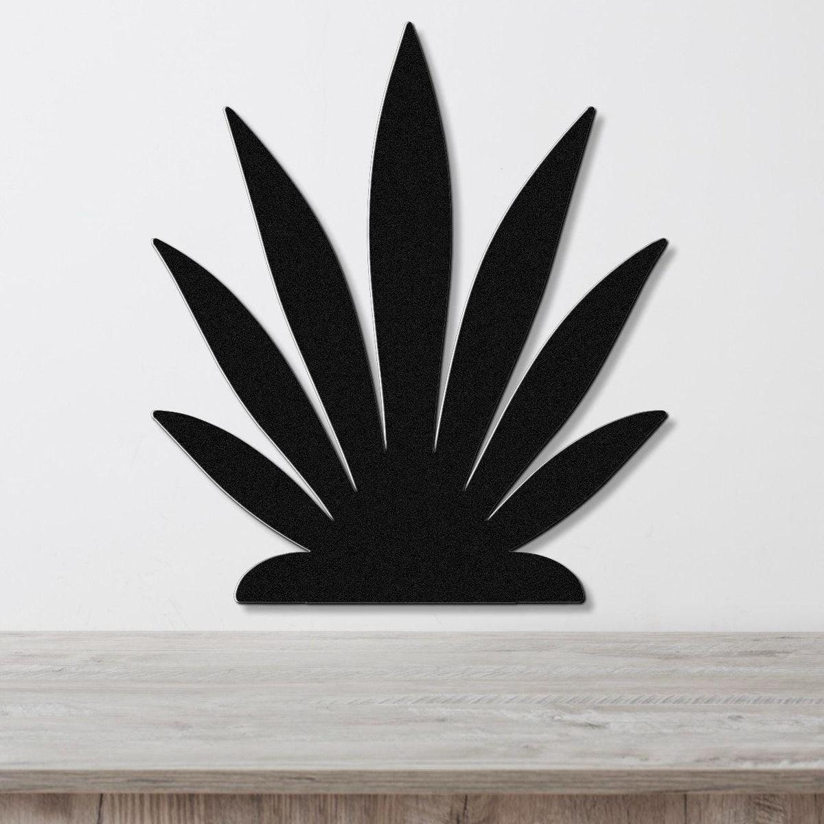 Black metal agave wall art with pointed leaf cutouts, mounted on a white wall above a light wood surface.