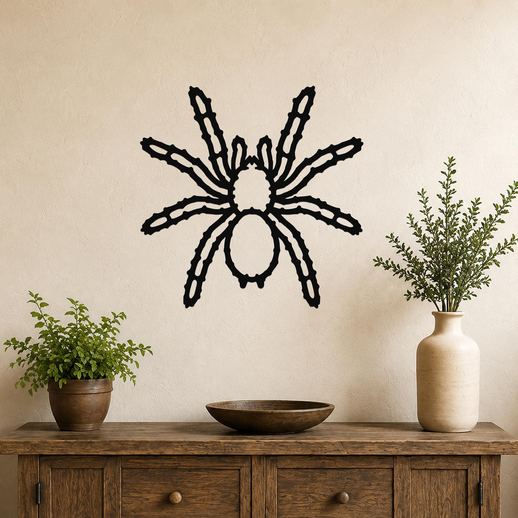 Black metal spider wall art with intricate leg cutouts, mounted on a beige wall above a wooden console table with potted plants.