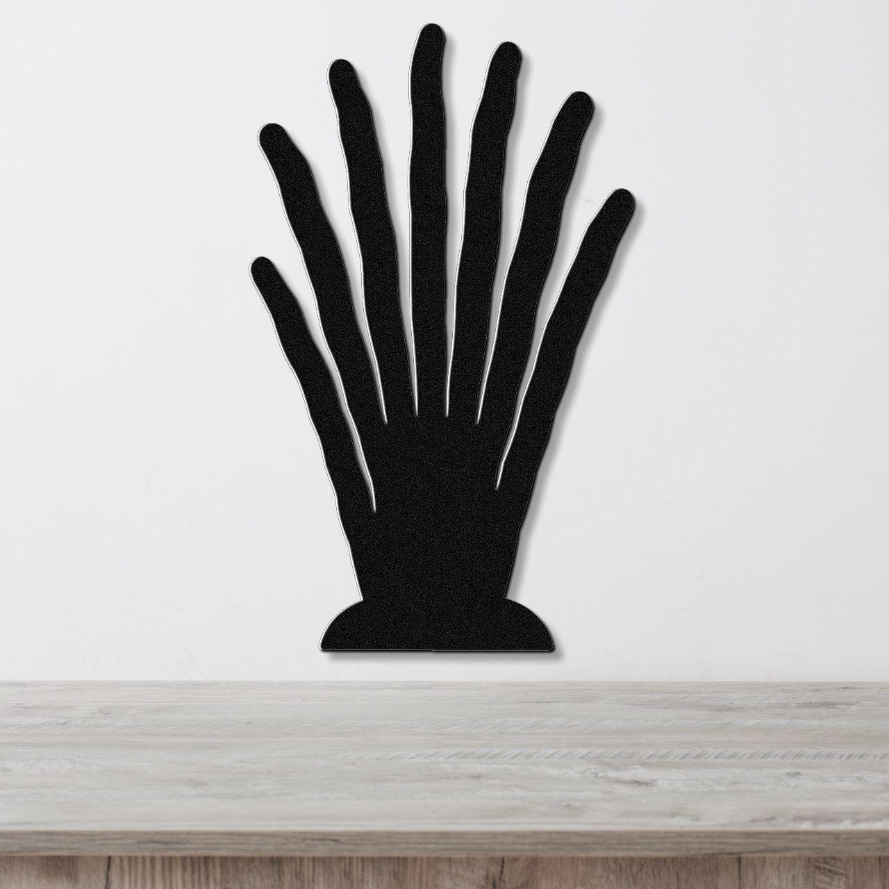 Black metal hand-shaped wall art with finger cutouts, mounted on a white wall above a light wood surface.