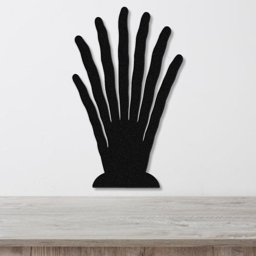 Black metal hand-shaped wall art with finger cutouts, mounted on a white wall above a light wood surface.