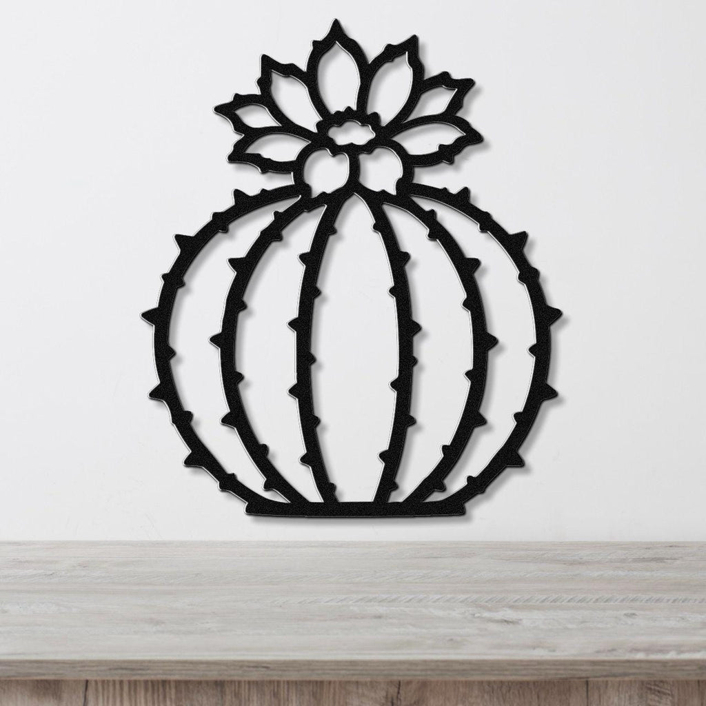 Black metal barrel cactus wall art with flower and spine cutouts, mounted on a white wall above a light wood counter.
