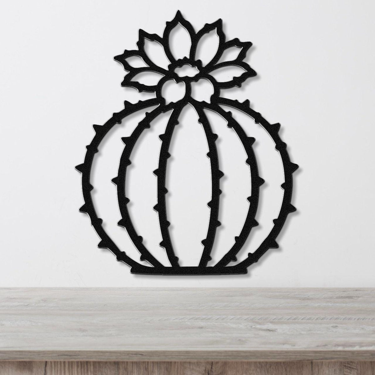 Black metal barrel cactus wall art with flower and spine cutouts, mounted on a white wall above a light wood counter.