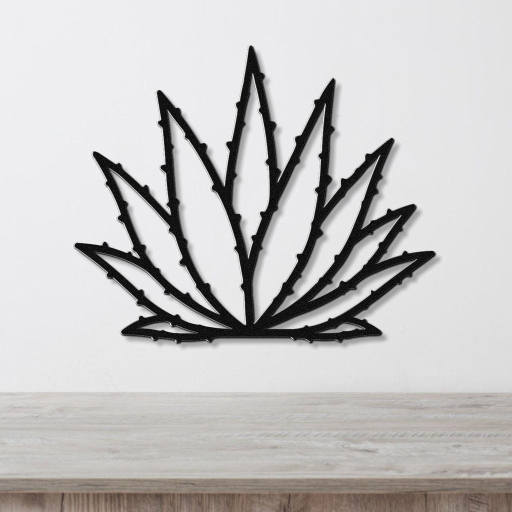 Black metal agave wall art with spiky leaf cutouts, mounted on a white wall above a light wood surface.