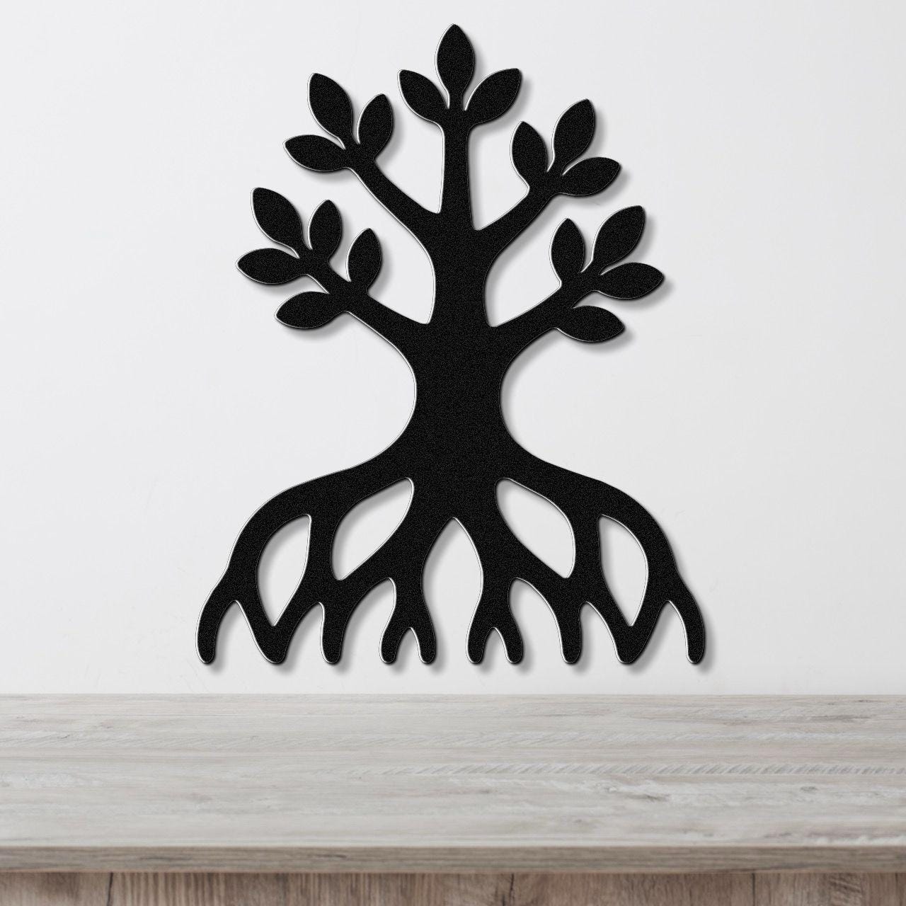 Black metal wall art in the shape of a tree with visible roots and leafy branches, mounted on a white wall above a wooden surface.