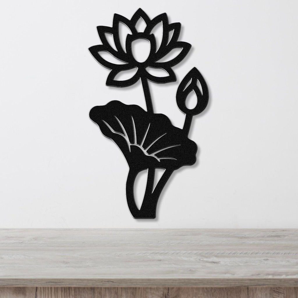 Black metal lotus flower wall art with cutout petals and leaves, mounted on a white wall above a wooden surface.