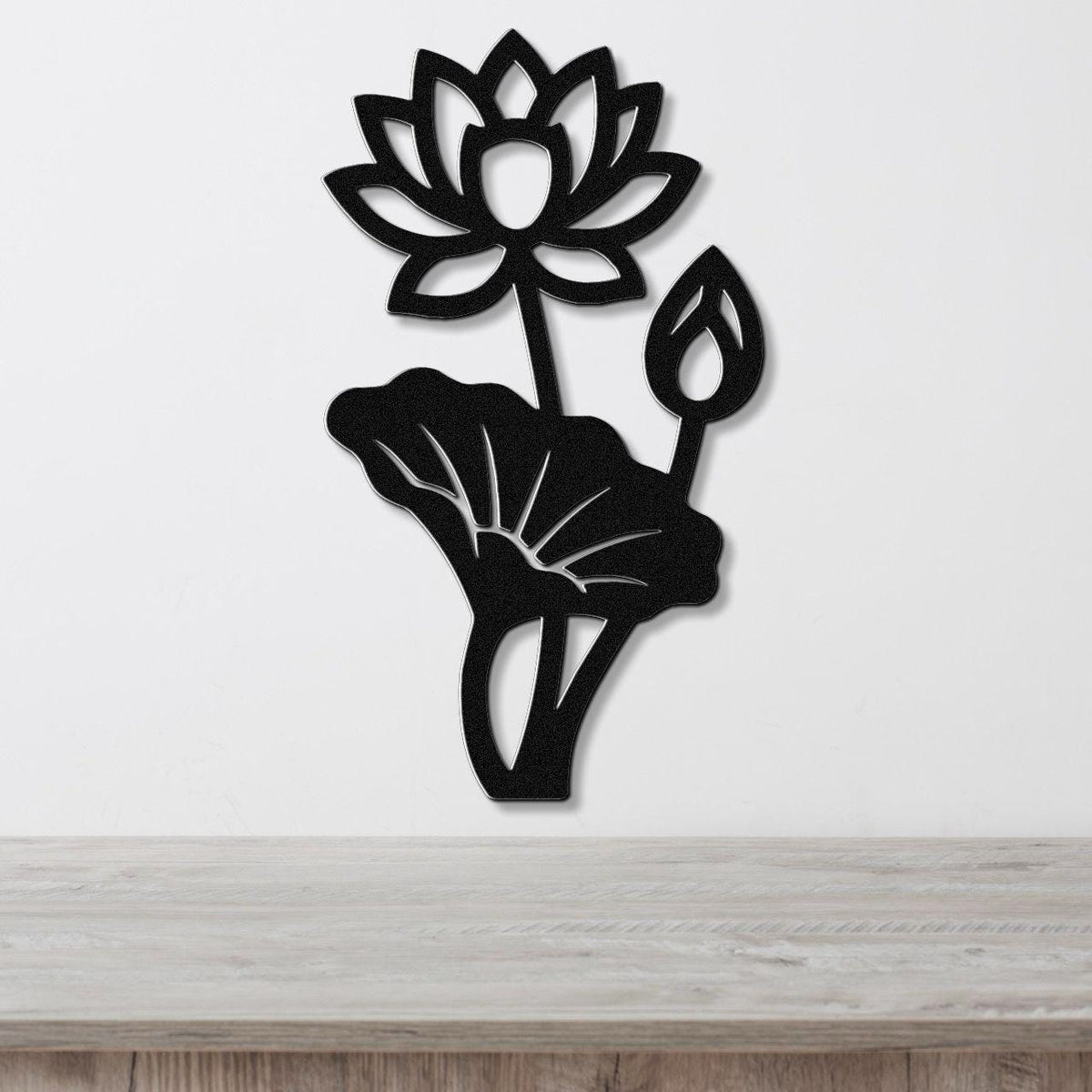 Black metal lotus flower wall art with cutout petals and leaves, mounted on a white wall above a wooden surface.