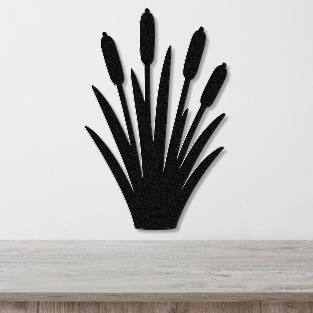 Black metal cattail wall art with a silhouette design of tall reeds and seed heads, mounted on a white wall above a light wood surface.
