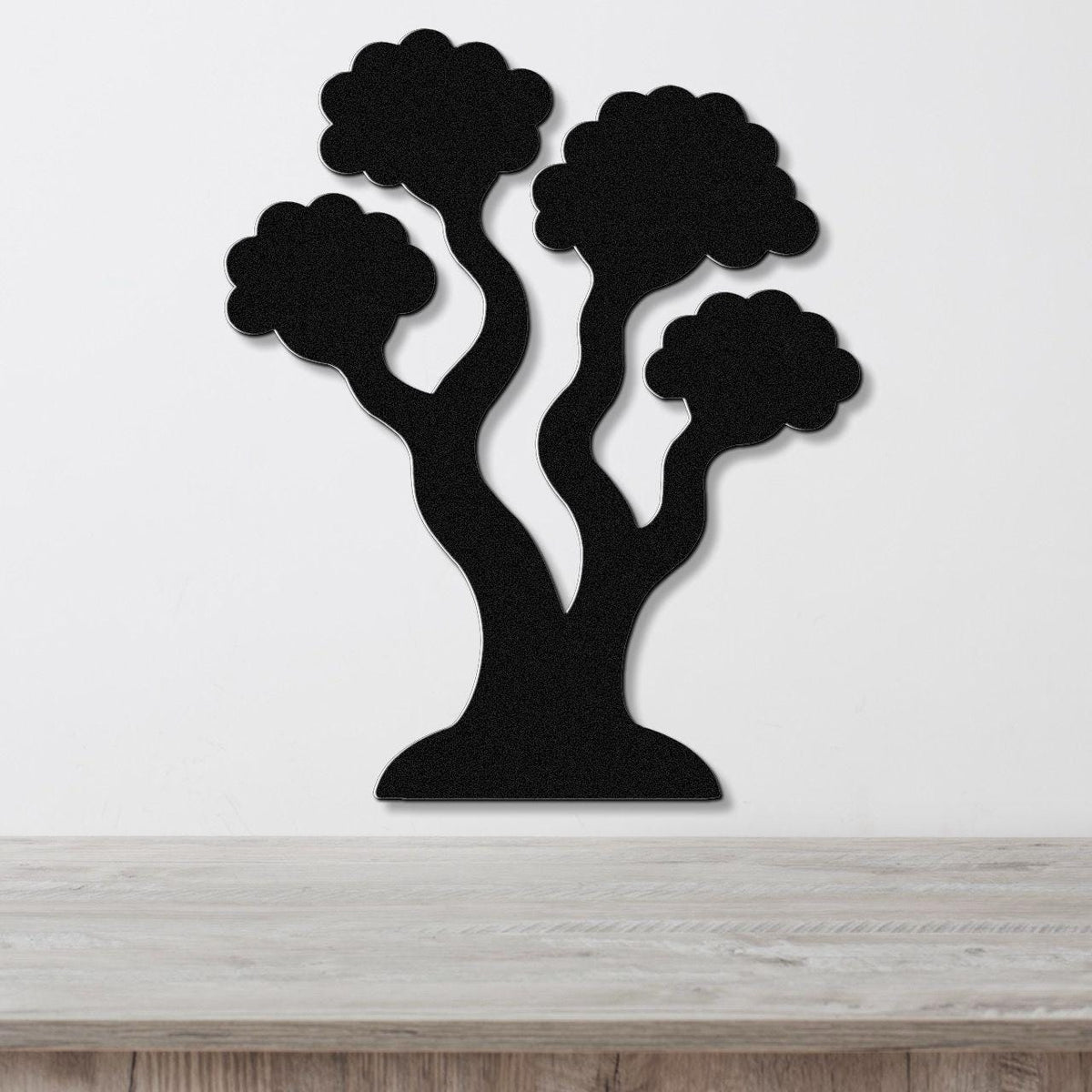 Black metal wall art in a stylized tree silhouette with three rounded canopies and curved trunks, mounted on a white wall above a light wood surface.